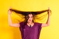 Young woman tangling her hair with her hands in disgust with her physical appearance, isolated on yellow background