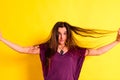 Young woman tangling her hair with her hands in disgust with her physical appearance, on yellow background