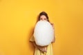 Young woman with tasty cotton candy on yellow