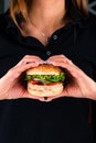 Young woman with tasty fast food unhealthy burger in hand hungry getting ready to eat heart-shaped hands Royalty Free Stock Photo