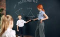 Young woman, teacher standing by blackboard with little boy, child and teaching math at school. Solving geometry tasks Royalty Free Stock Photo