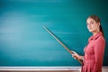 Young woman teacher stands at a blackboard with a pointer. Template for the school timetable and other information.