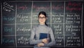 Young woman teacher or student, wearing eyeglasses and holding a book, stands in front of blackboard written with chalk english Royalty Free Stock Photo