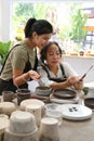 Young woman teaching mature woman making handicraft crockery in pottery workshop