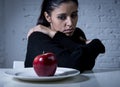 Young woman or teen looking apple fruit on dish as symbol of crazy diet in nutrition disorder Royalty Free Stock Photo