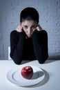 Young woman or teen looking apple fruit on dish as symbol of crazy diet in nutrition disorder Royalty Free Stock Photo