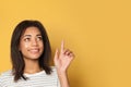 Young woman teen pointing her finger up on yellow background, studio portrait