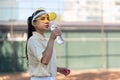 Young woman tennis player on the court drinking water. Recreation after hard exercises. Sportive girl in sun hat drinks Royalty Free Stock Photo