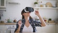 Young woman is testing virtual reality glasses in kitchen at home.