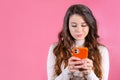 Young woman texting someone unhappily using smartphone on the pink background Royalty Free Stock Photo