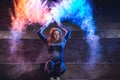 Young woman throws and dance with color powder on dark background