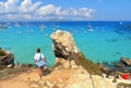 Young woman on the top of the rock cliff looks at paradise clear torquoise blue water with boats and cloudy blue sky in background Royalty Free Stock Photo