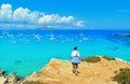 Young woman on the top of the rock cliff looks at paradise clear torquoise blue water with boats and cloudy blue sky in background Royalty Free Stock Photo