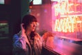 Young woman touching her hair looking through the glass next to a club with a window with neon lights take away