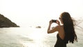 Woman tourist on beach island taking photograph of sunset with smartphone on holiday of boat and skyline view Royalty Free Stock Photo