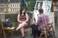 Young woman, tourist, being drawn and painted as a caricature by a portrait caricaturist on Charles bridge, a major landmark