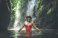 Young woman tourist with straw hat and red swimsuit in the deep jungle with waterfall. Real adventure concept. Bali Royalty Free Stock Photo