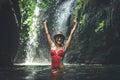 Young woman tourist with straw hat and red swimsuit in the deep jungle with waterfall. Real adventure concept. Bali Royalty Free Stock Photo