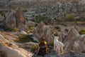 A young woman tourist in a hat and dog sit on a mountain and looks at the sunrise in Cappadocia. Turkey. Top attraction travel des