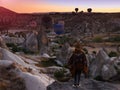 A young woman tourist in a hat standing on a mountain and looks at the sunrise and balloons in Cappadocia. Turkey. Top attraction.