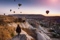 A young woman tourist in a hat standing on a mountain and looks at the sunrise and balloons in Cappadocia. Turkey. Top attraction.