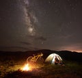 Woman resting at night camping near campfire, tourist tent, bicycle under evening sky full of stars Royalty Free Stock Photo