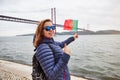 Young woman tourist holding the flag of Portugal in hands and enjoying landscape view on the famous iron bridge 25th of April Royalty Free Stock Photo