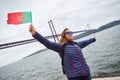 Young woman tourist holding the flag of Portugal in hands and enjoying landscape view on the famous iron bridge 25th of April Royalty Free Stock Photo
