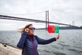 Young woman tourist holding the flag of Portugal in hands and enjoying landscape view on the famous iron bridge 25th of April Royalty Free Stock Photo