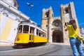 Woman tourist photographing retro yellow tram 28 on the street in Lisbon in front of Santa Maria cathedral, Portugal Royalty Free Stock Photo