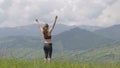 Young woman tourist raising her hands in winner gestion while hiking in summer mountains.