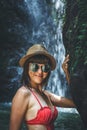 Young woman tourist in red swimsuit and straw hat posing in the deep jungle with waterfall. Real adventure concept. Bali Royalty Free Stock Photo