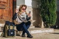 Young woman tourist sits on street on steps, looking for path on map, next to her backpack. Tourism, travel, vacation.