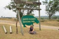 Young woman tourist sitting under the sign of Queen Elizabeth National Park