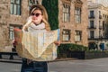 Young woman tourist stands on street of ancient European city and holds map. In background is beautiful building. Royalty Free Stock Photo