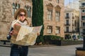 Young woman tourist stands on street of ancient European city and holds map. In background is beautiful building. Royalty Free Stock Photo