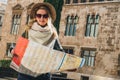 Young woman tourist stands on street of ancient European city and holds map. In background is beautiful building. Royalty Free Stock Photo