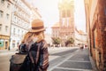 Young woman tourist in straw hat and backpack uses phone as navigator through streets of Europe