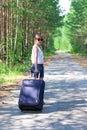 young woman tourist with a suitcase on a forest road on a summer sunny day against the backdrop of green trees. Close-up. Selecti Royalty Free Stock Photo