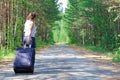 young woman tourist with a suitcase on a forest road on a summer sunny day against the backdrop of green trees. Close-up. Selecti Royalty Free Stock Photo