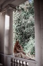 Young woman tourist in summer dress is sitting with her bare feet on ancient balustrade of old palace terrace, pavilion