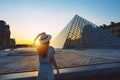 Young woman tourist in sun hat standing in front of Louvre museum in Paris at sunset. Travel in France, tourism concept Royalty Free Stock Photo