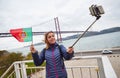 Young woman tourist take selfies on the background of famous iron 25th of April bridge and holding the flag of Portugal in hands Royalty Free Stock Photo