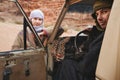 Young woman in traditional Bedouin coat - bisht - and headscarf, sitting next to old 4wd vehicle, looking over opened door,