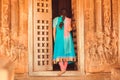 Young woman in traditional sari open the door of Hindu temple with stone wall relief, India. Carved architecture of Asia