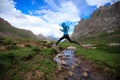 Woman trail runner jumping over stream water at mountain