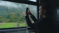 Young woman in train. Girl takes photo of mountain landscape outside the window while sitting inside transport