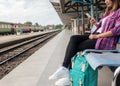 Young woman traveler and backpack waiting railway at train station, Young woman sitting with using smartphone at train station