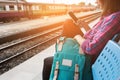 Young woman traveler and backpack waiting railway at train station, Young woman sitting with using smartphone at the train station