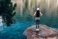Young woman traveler in grey pants standing back to the camera on the big rock near the beautiful mountain lake, active Royalty Free Stock Photo